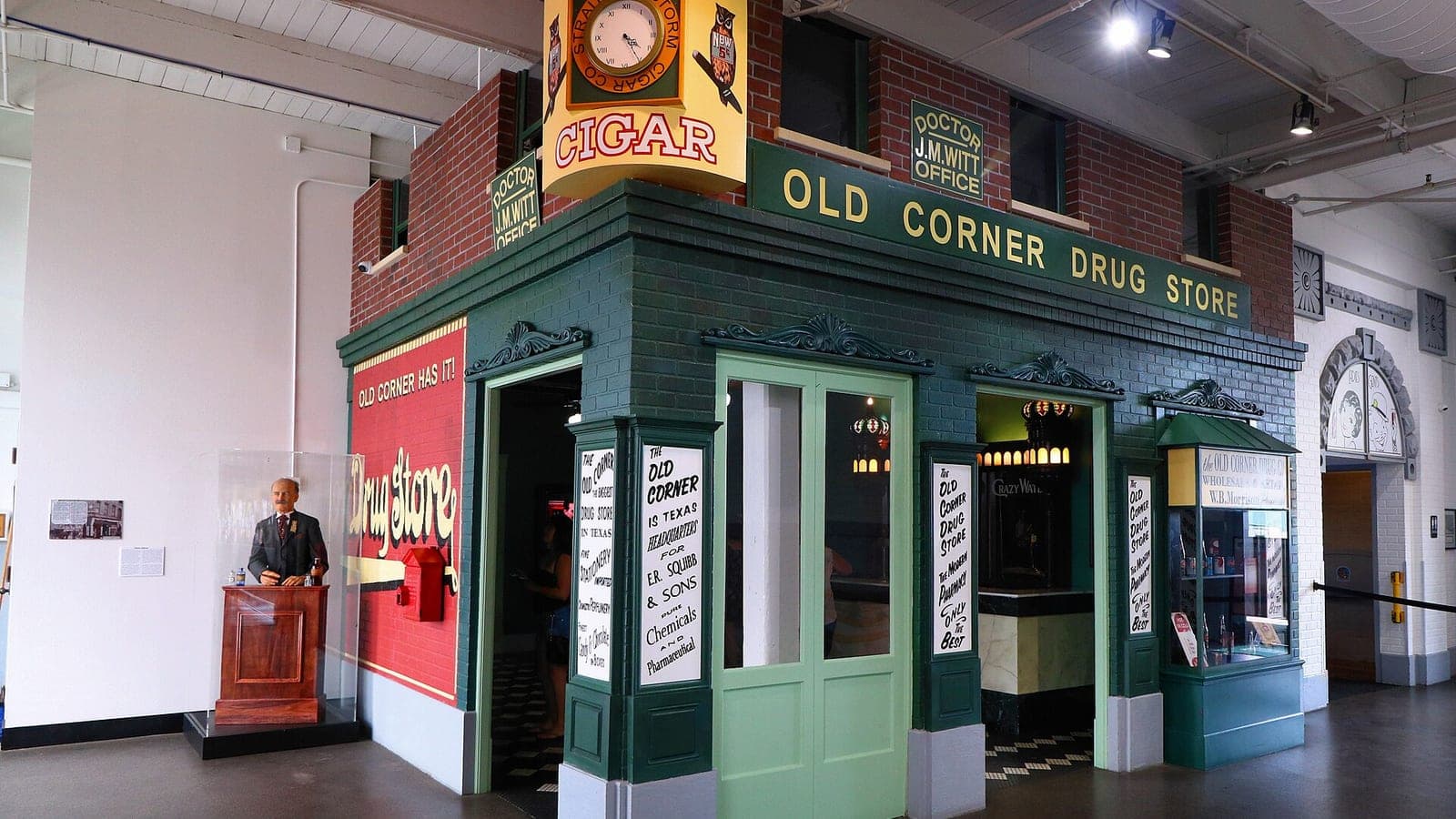 The Old Corner Drug Store exhibit inside the Dr Pepper Museum: a green and brick storefront with an Owl Cigar clock sign above the door